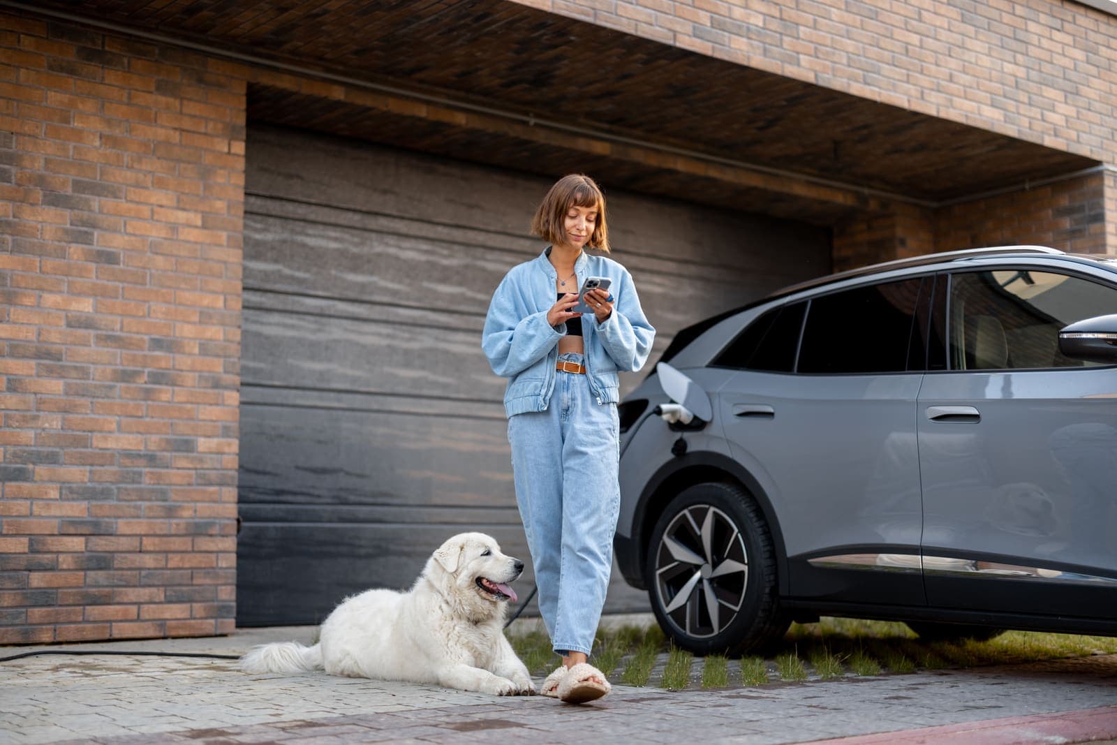 Woman with her dog beside a charging electric car at home